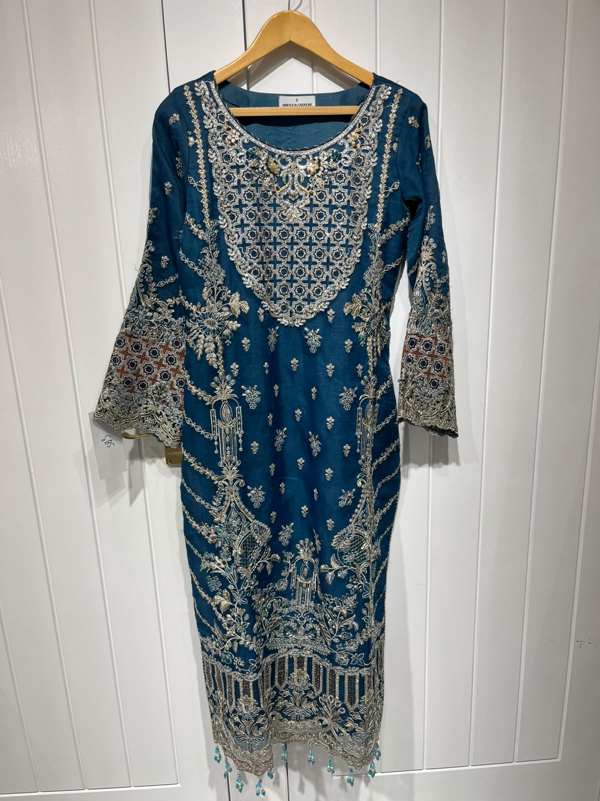 A teal blue ensemble with an ornate embroidered neckline, floral…