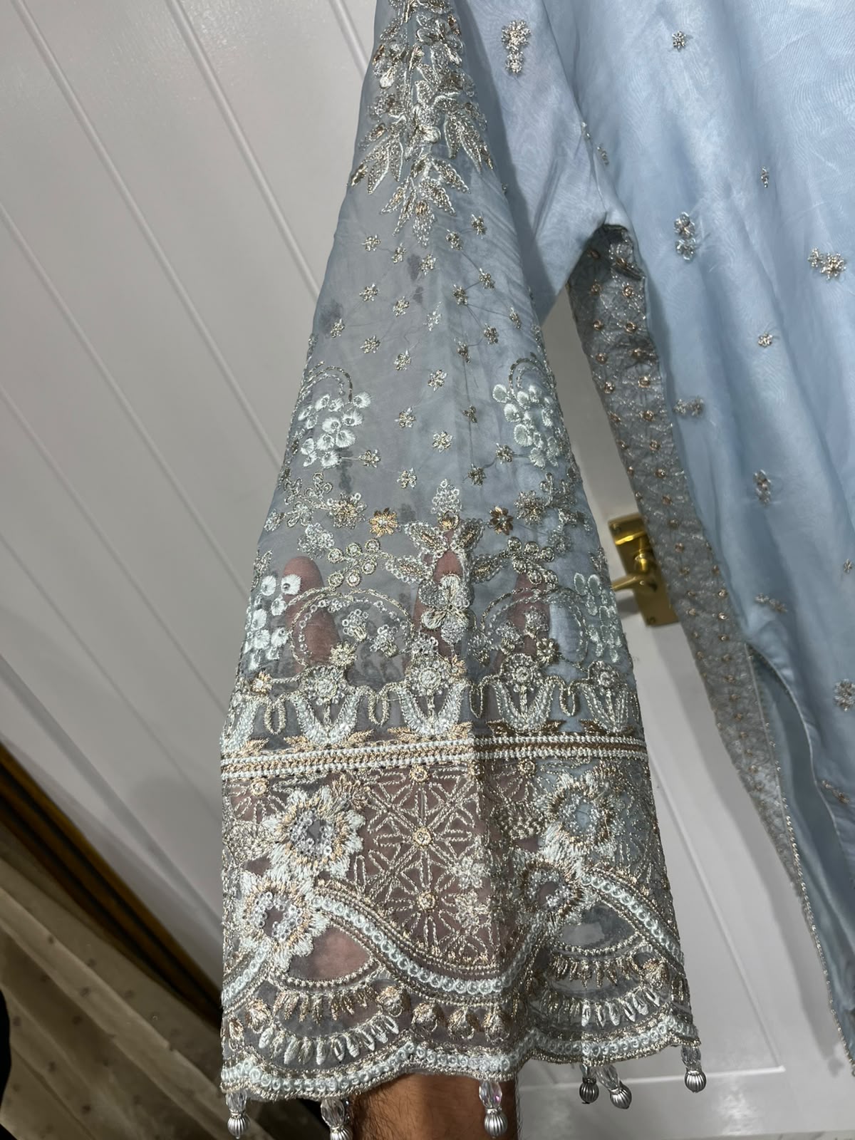 An ice blue ensemble with intricate metallic-toned embroidery, ornate…