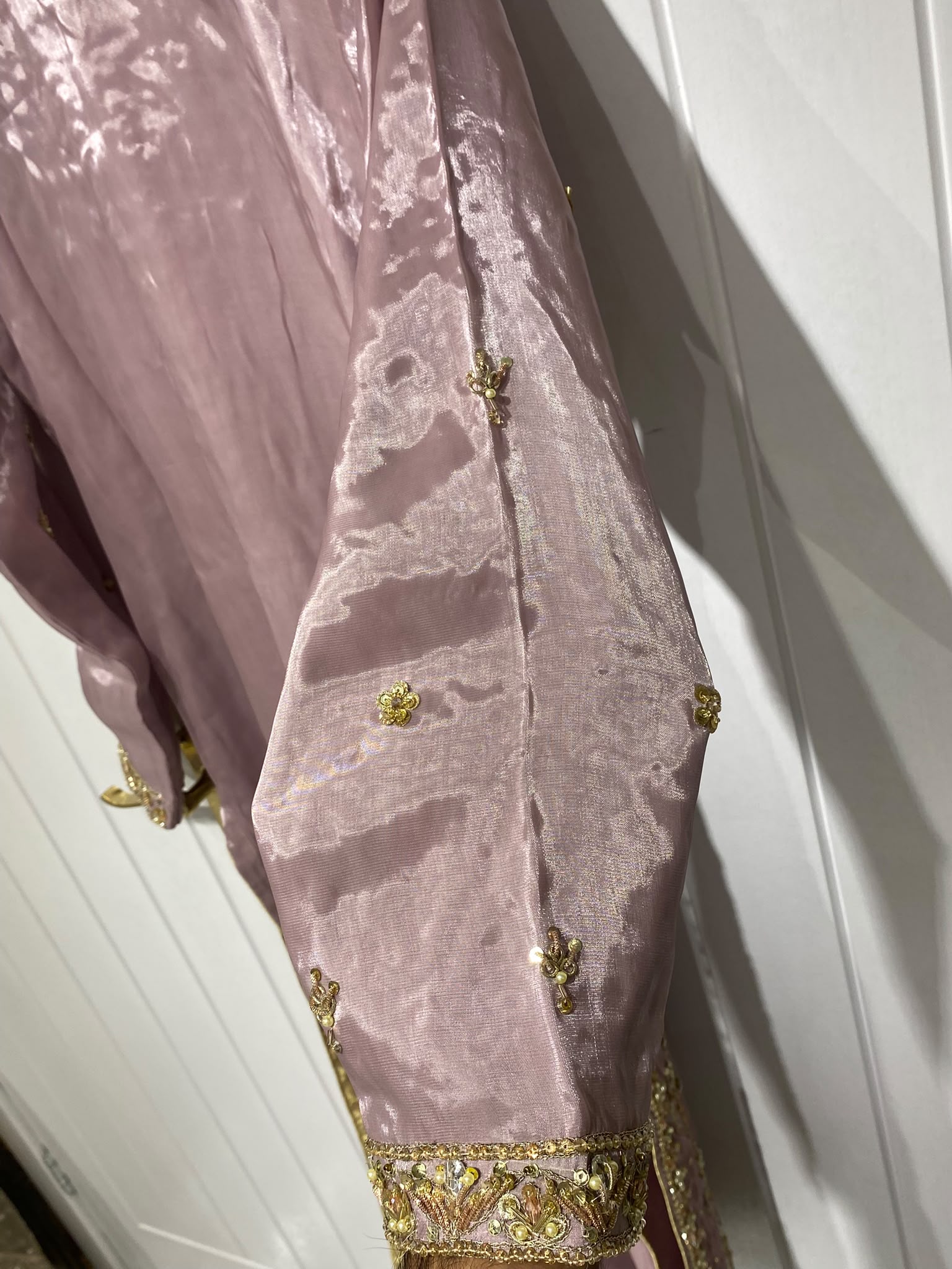 A dusty mauve ensemble with a long gold-toned neckline, vertical…
