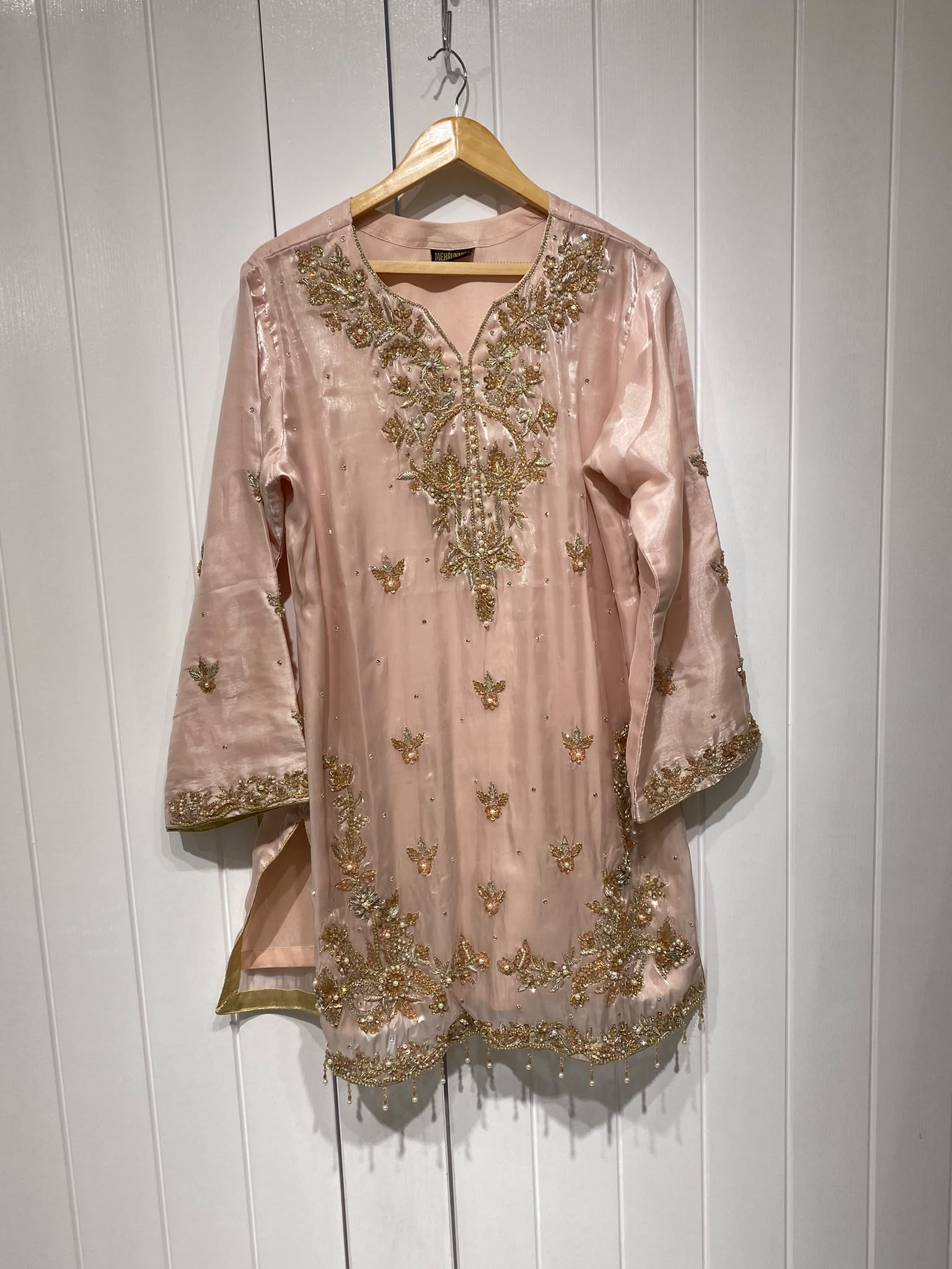 A blush pink shirt with a statement gold-toned neckline, scattered…