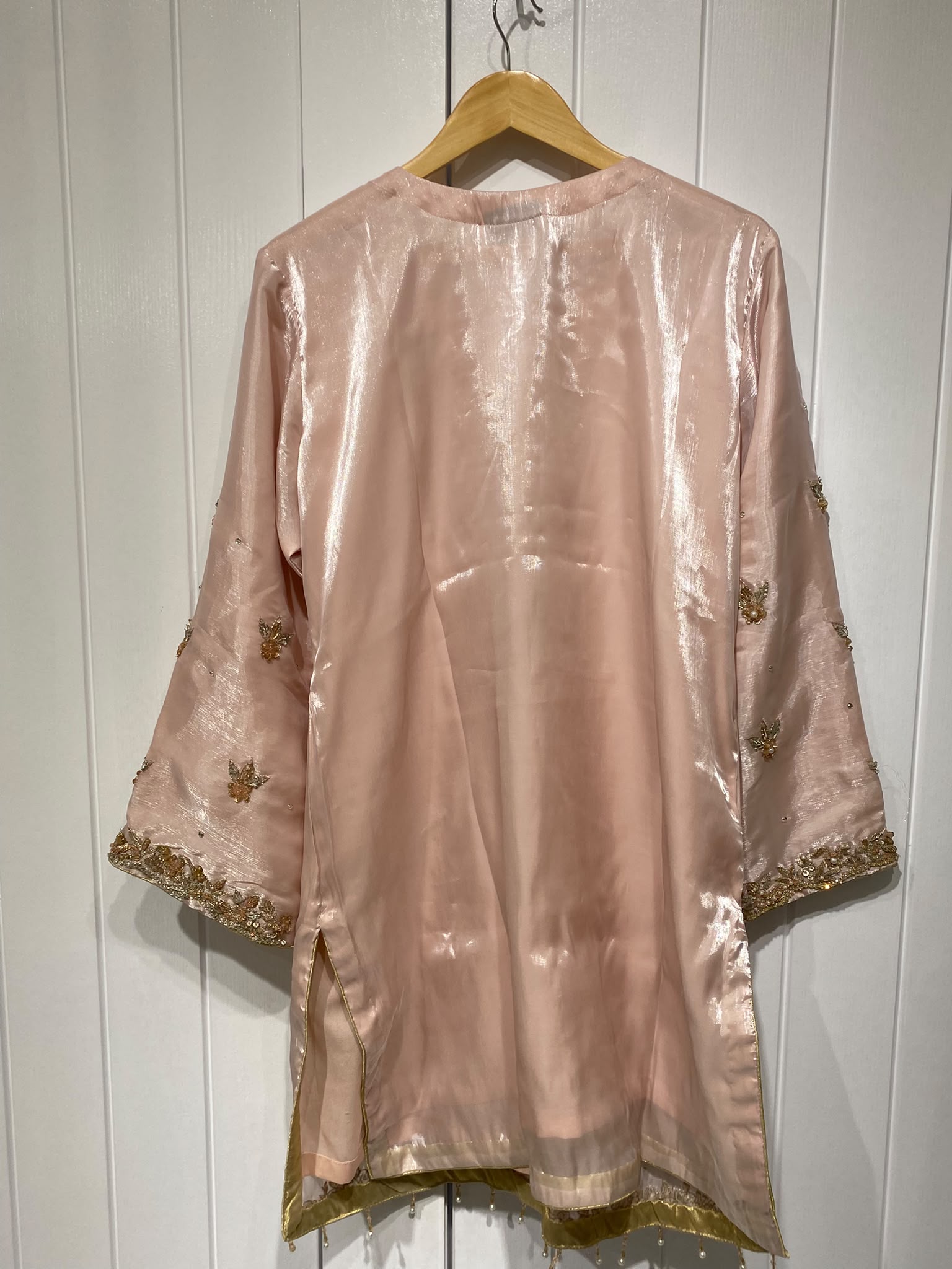 A blush pink shirt with a statement gold-toned neckline, scattered…
