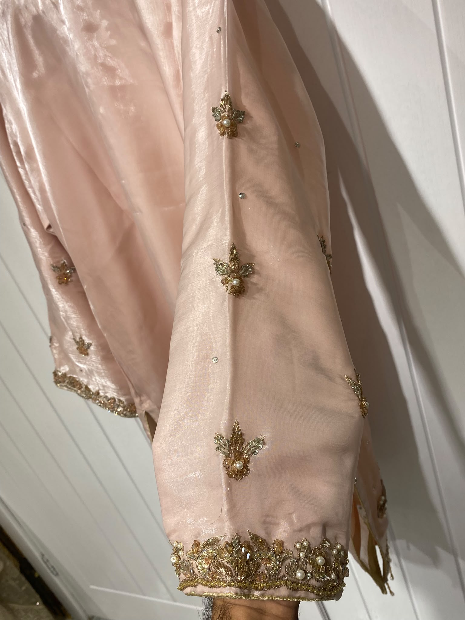 A blush pink shirt with a statement gold-toned neckline, scattered…
