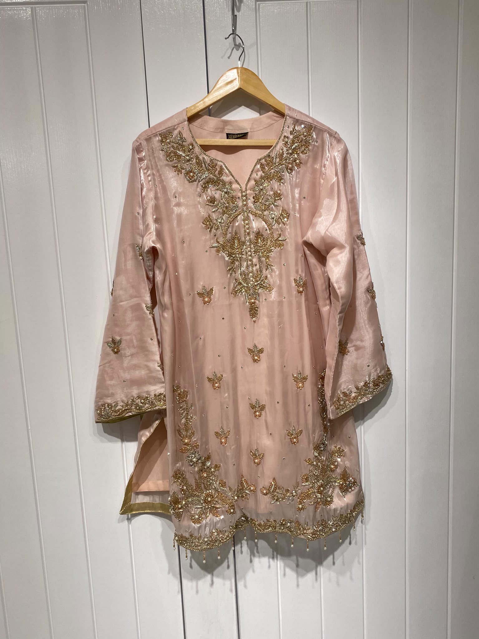 A blush pink shirt with a statement gold-toned neckline, scattered…